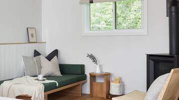 A modern bedroom with a green sofa bed, a wooden chair, a small table with a vase, and a fireplace.