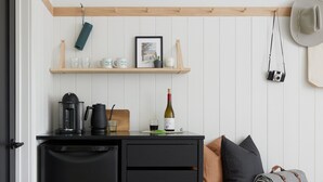 Cocina compacta con un refrigerador negro, una cafetera, una botella de vino y un estante de madera sobre la encimera.