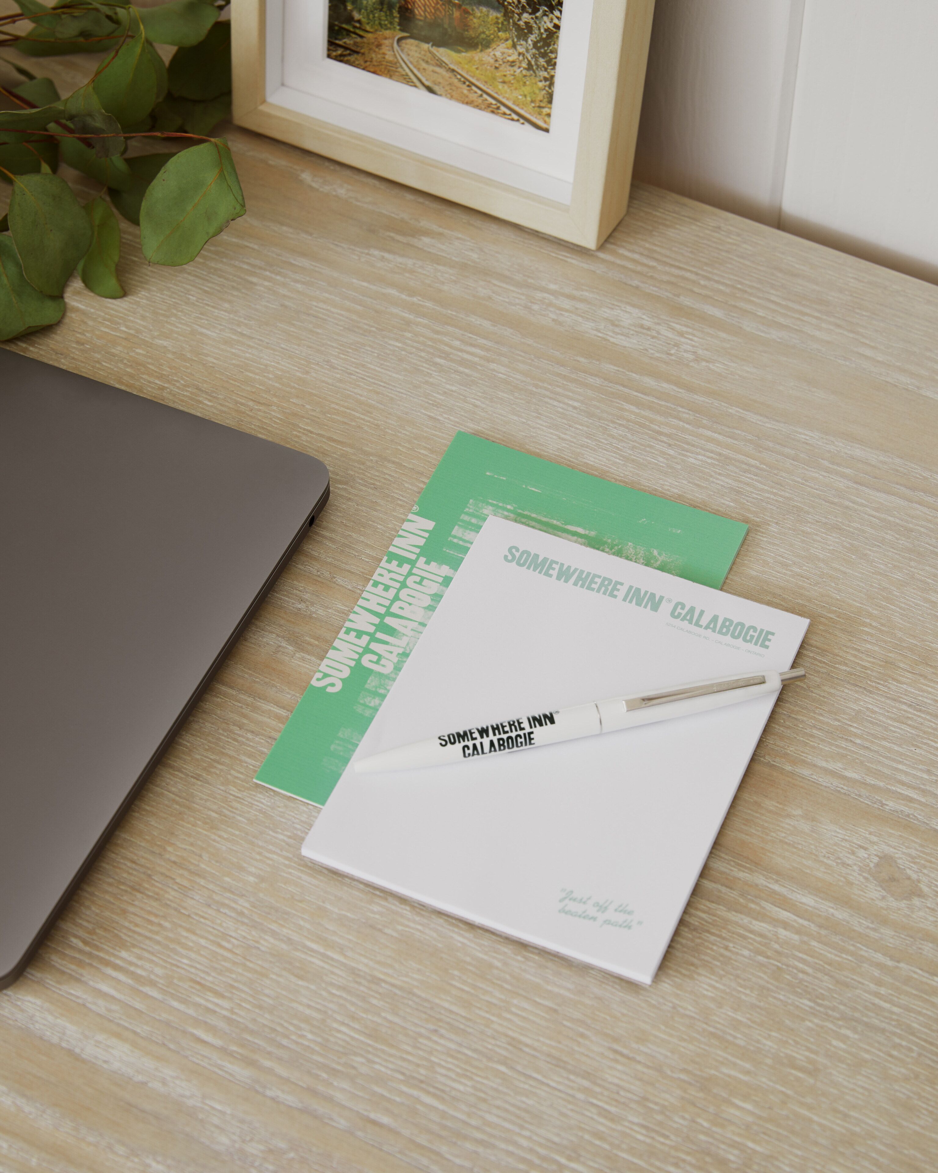 A laptop, a notebook, and a pen on a wooden surface.