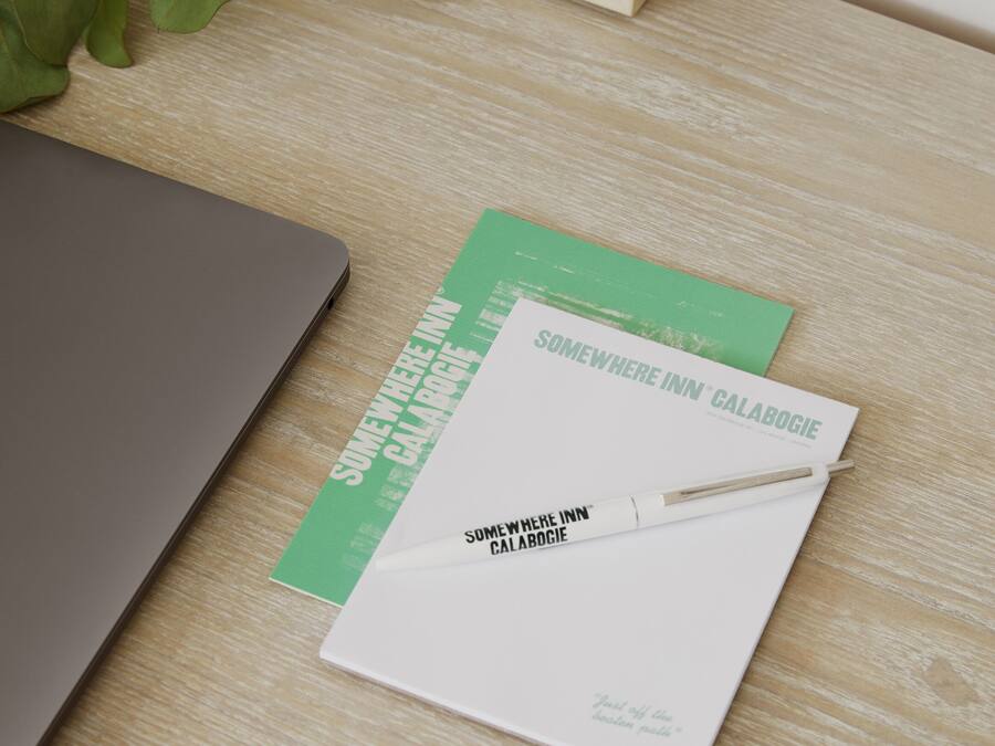 A laptop, a notebook, and a pen on a wooden surface.