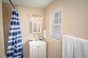 Bathroom features a shower curtain, sink, mirror, and window with blinds.