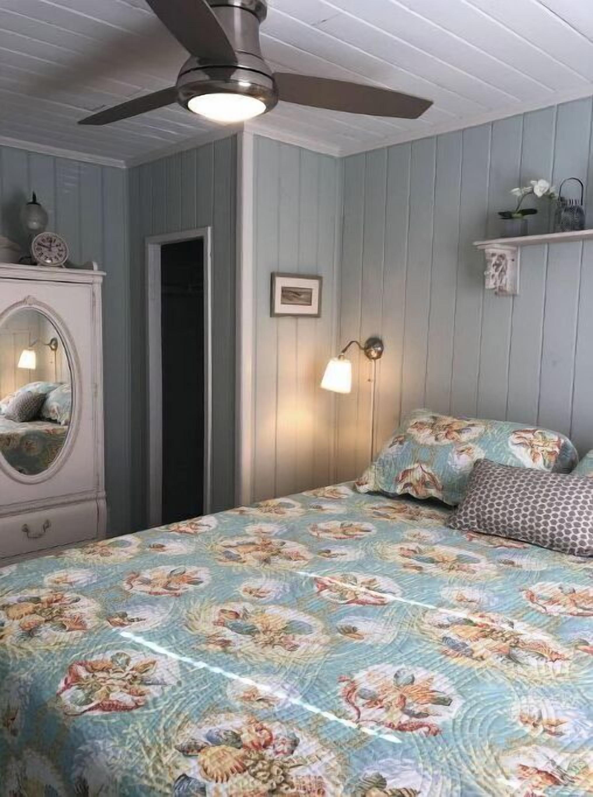 A bedroom with a bed, a ceiling fan, a dresser, and a wall-mounted light fixture.