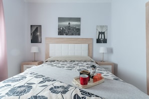 Un dormitorio ordenado con una cama, dos mesitas de noche y una obra de arte con un paisaje urbano en la pared.