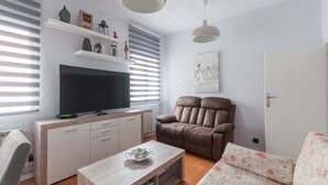 Una sala moderna con una televisión de pantalla plana, un sillón reclinable marrón, un sofá estampado, una mesa de centro de madera y un armario blanco.
