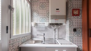 Una cocina compacta con un lavamanos, una ventana con persianas y baldosas estampadas en las paredes.