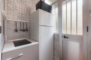 Una cocina compacta con un refrigerador blanco, una pequeña encimera y utensilios colgantes.