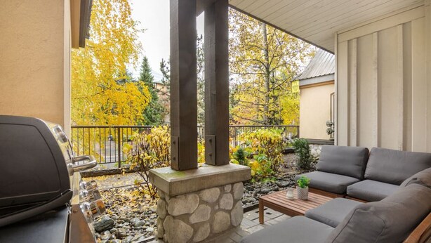 An outdoor patio with a stone fireplace, a grill, and a gray sofa. - NEW! 2BR Townhouse: Private HotTub, Free Parking (Whistler)