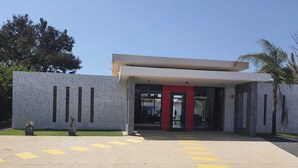 A modern building with a flat roof, large windows, and a red door. There are yellow tactile paving tiles in front. - Villa saly joseph (M'bour)