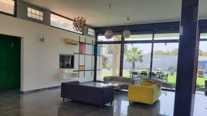 A spacious living area with a large window, a sofa, a yellow ottoman, and a flat-screen TV mounted on the wall. - Villa saly joseph (M'bour)