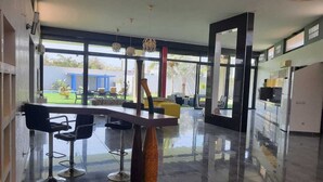A modern kitchen with a central island, bar stools, and large windows offering a view of the outdoors. - Villa saly joseph (M'bour)
