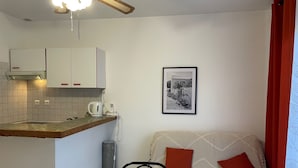 Een knus woongedeelte met een kitchenette, een eethoek en een bank met rode kussens.