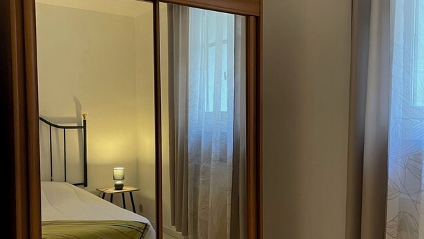 Een hotelkamer met een bed, nachtkastje, spiegel en raam met gordijnen.