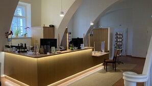 A reception desk with a wooden finish, a potted plant, and a window with a view of trees. - Zentrum-Kloster-Lehnin (Kloster Lehnin)