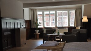 A hotel room with a bed, a desk, a chair, a lamp, and a view of a brick building through large windows. - Zentrum-Kloster-Lehnin (Kloster Lehnin)