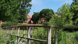 A rustic wooden fence with a brick building in the background, surrounded by lush greenery and a clear blue sky. - Zentrum-Kloster-Lehnin (Kloster Lehnin)