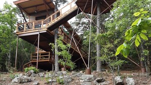 Una casa en árbol con varios niveles unidos por pasarelas de madera, rodeada de árboles y terreno rocoso.