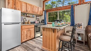 Una cocina con armarios de madera, un refrigerador blanco, una estufa y un amplio ventanal con cortinas.