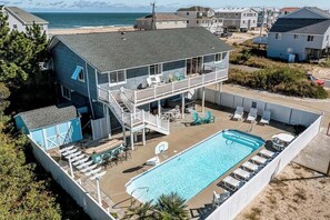 Une maison à deux étages dotée d’un balcon donnant sur une plage, d’une piscine et d’un espace salon extérieur.