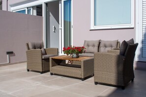 Un patio exterior con mobiliario de mimbre, una mesa con un jarrón de flores y una puerta corrediza de vidrio.