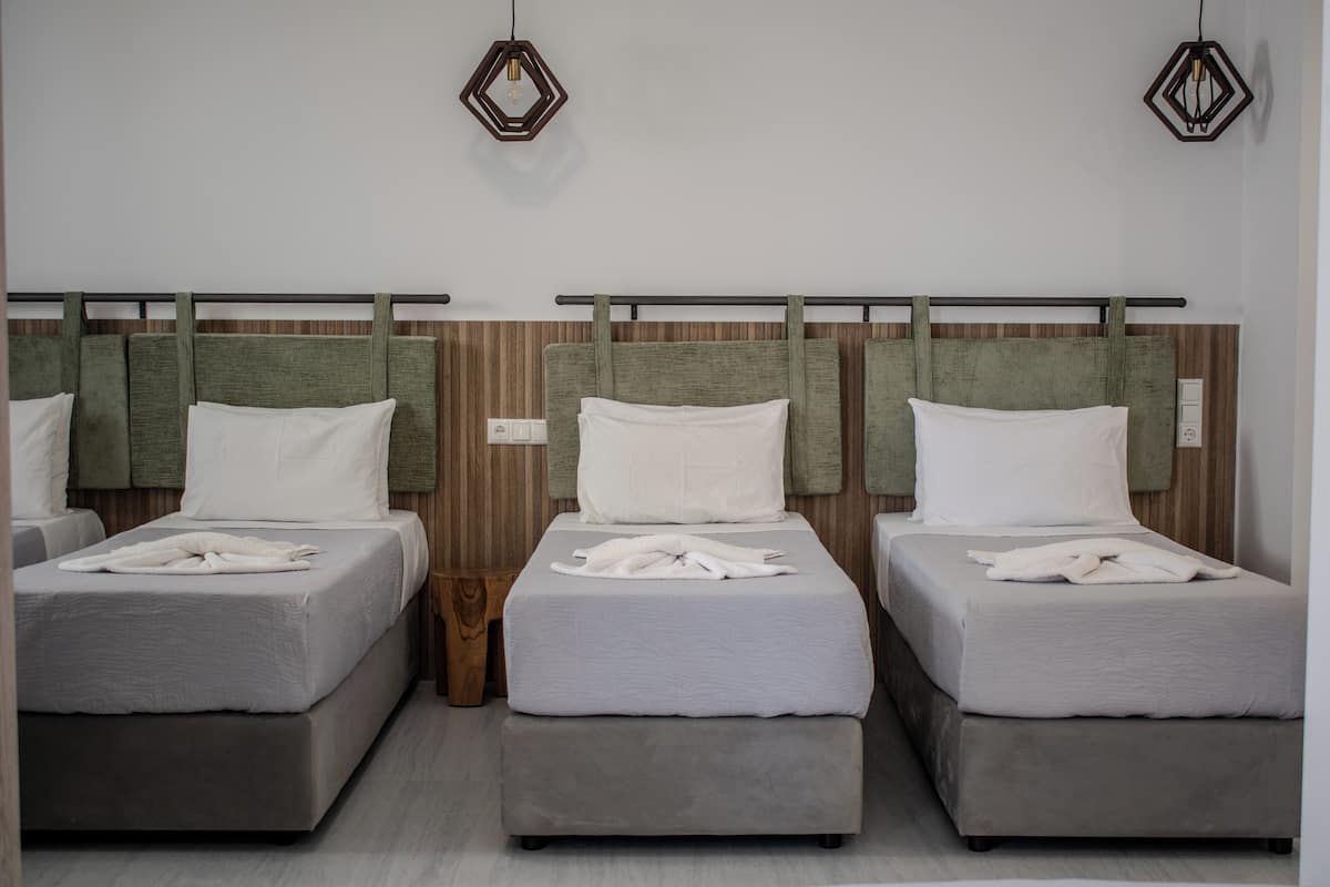 Tres camas con ropa de cama gris, cabeceros de madera y suelo de madera.