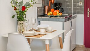 A dining table with white chairs, a vase with red roses, and a fruit bowl on the counter. - La Fleur (Skiathos)