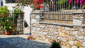 A stone-paved courtyard with a stone wall and metal railing. - La Fleur (Skiathos)
