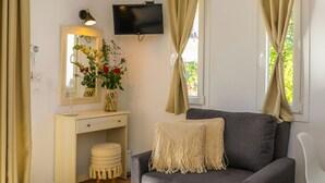 A modern living room with a grey sofa, beige curtains, a flat-screen TV, a small desk with a mirror, and a vase with flowers. - La Fleur (Skiathos)