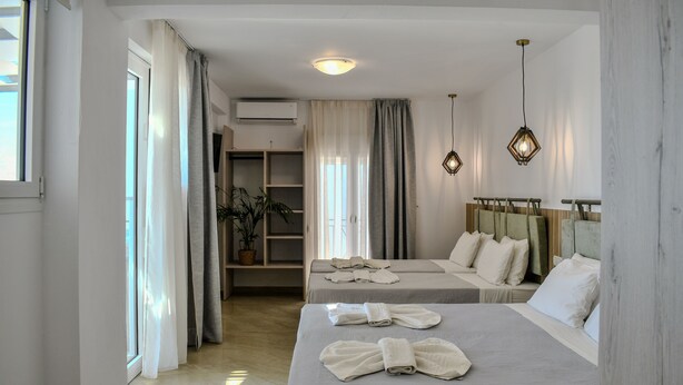 A hotel room with two beds, a wardrobe, a potted plant, and a view of the outside. - La Fleur (Skiathos)