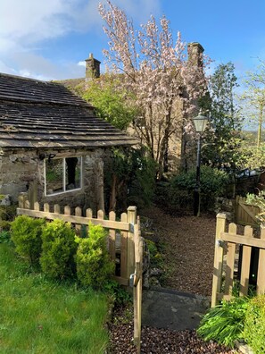 A stone cottage with a wooden gate, surrounded by greenery and a flowering tree. - Cottage with pretty garden and views. 2 mins from cobbled square, pubs/amenities (Skipton)