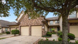 A two-story house with a stone facade, beige garage doors, and a well-maintained front yard with shrubs and a tree. - Spacious Townhome With KING SUITE&Spa Tub (Houston)