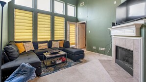 A living room with a sectional sofa, a fireplace, and large windows with blinds. - Spacious Townhome With KING SUITE&Spa Tub (Houston)