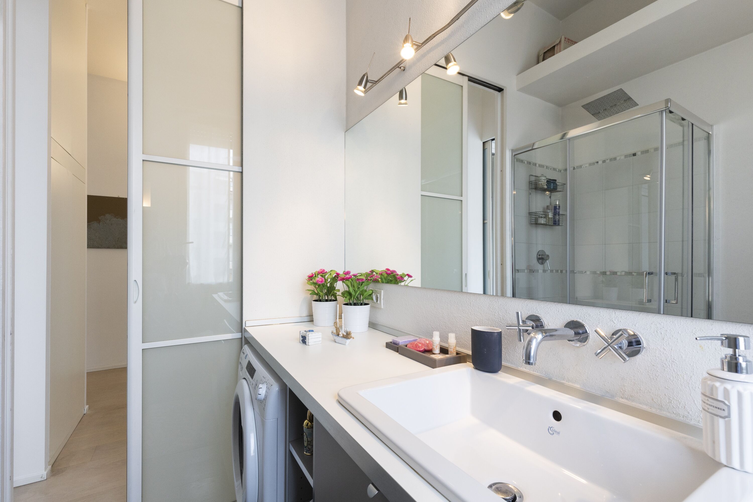A modern bathroom with a large mirror, white sink, and a glass shower enclosure.