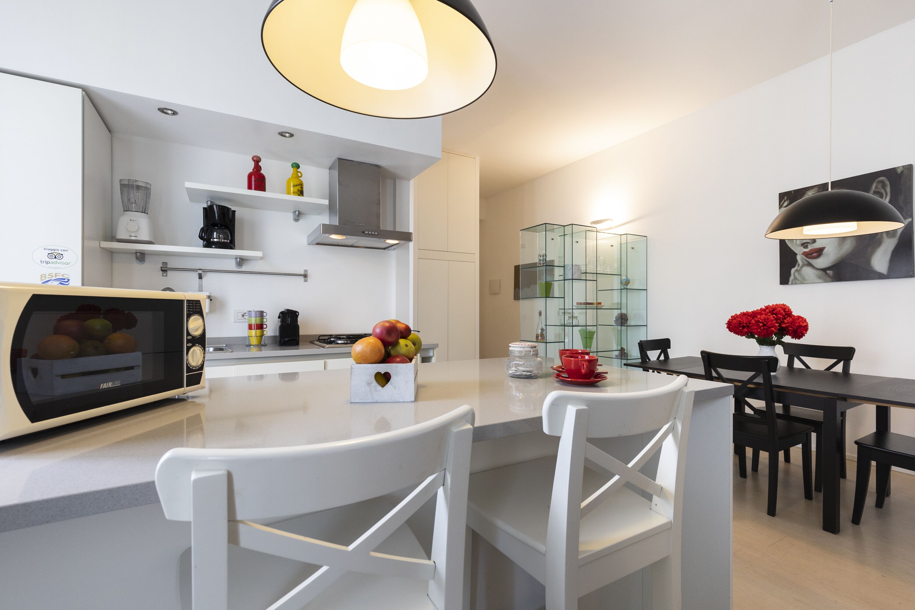 Une cuisine moderne dotée d’un four encastré, de chaises blanches, d’une table à manger et d’un meuble vitrine en verre.