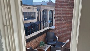 A balcony with two chairs and a small table, a brick wall, and a view of buildings in the background.