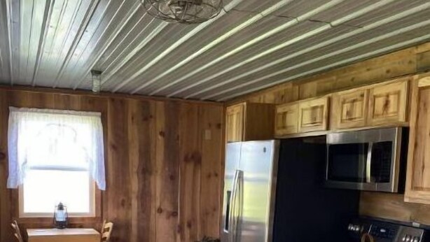A compact kitchen with wooden cabinets, a stainless steel refrigerator, a microwave, and an oven. - S and H Tack Room Enjoy a peaceful getaway (Sparta)