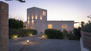 A modern building with a paved driveway, well-lit exterior, and surrounding greenery. - Perivoli SeaView Cottage, a Rural Bliss of Nature, Close to tavernas & beach (Rethymno)