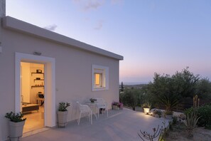 Uma casa moderna com um espaço de pátio com mesa e cadeiras, plantas em vasos e vista para a paisagem.