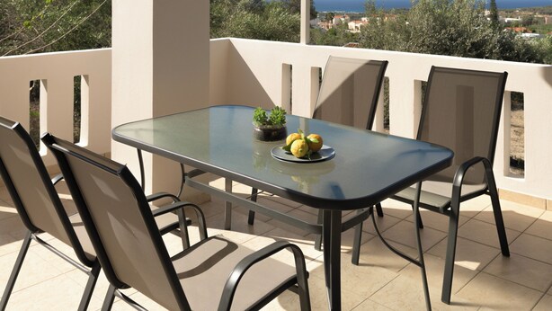 A balcony with a glass table, chairs, and a potted plant. - Perivoli SeaView Cottage, a Rural Bliss of Nature, Close to tavernas & beach (Rethymno)