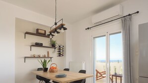 A modern kitchen with a wooden table, black chairs, and a hanging light fixture. There are shelves with decorative items and a potted plant. - Perivoli SeaView Cottage, a Rural Bliss of Nature, Close to tavernas & beach (Rethymno)