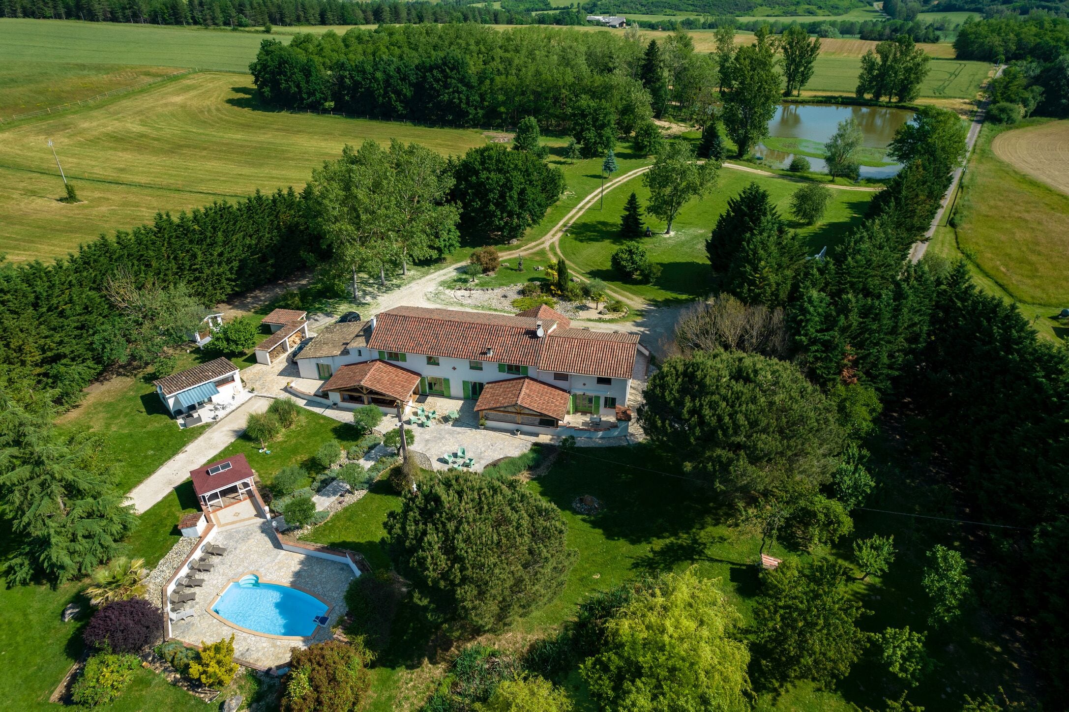 Vue aérienne d’une propriété comprenant une grande maison, une piscine et de nombreux espaces verts.