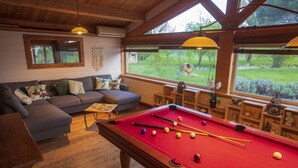 A cozy room with a pool table, a sofa, and a view of a garden. - Au Temps Suspendu - Large Gîte 16 People - Pyrenees (Saint-Martin-d'Oydes)