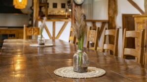 A wooden dining table with a glass vase containing dried plants, surrounded by wooden chairs. - Au Temps Suspendu - Large Gîte 16 People - Pyrenees (Saint-Martin-d'Oydes)