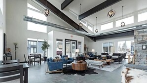 A spacious living area with a high ceiling, modern furniture, and a stone fireplace. - LUX Modern Retreat: Hot tub & Pool, Perfect Location! (Whitefish)