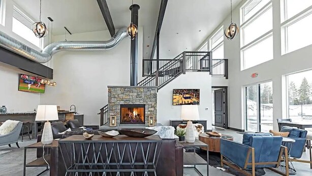 A spacious living area with a stone fireplace, comfortable seating, and a staircase leading to an upper level. - LUX Modern Retreat: Hot tub & Pool, Perfect Location! (Whitefish)
