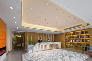 Un espace d’accueil d’hôtel comprenant un comptoir de réception en marbre, un autre en bois, et une bibliothèque avec des cadres contenant des photos.