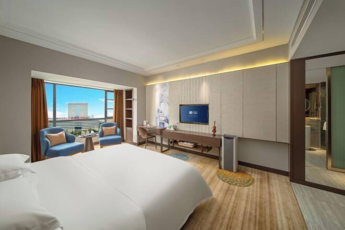 Ein Hotelzimmer mit einem großen Bett, einem Schreibtisch, einem Fernseher und Blick auf die Stadt.