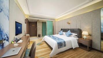 A modern hotel room with a large bed, a desk with a laptop, a TV, and a mirror.