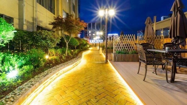 Ein Patio im Freien bei Nacht mit einem gepflasterten Weg, Sitzgelegenheiten mit Tischen und Stühlen und einem dekorativen Zaun.