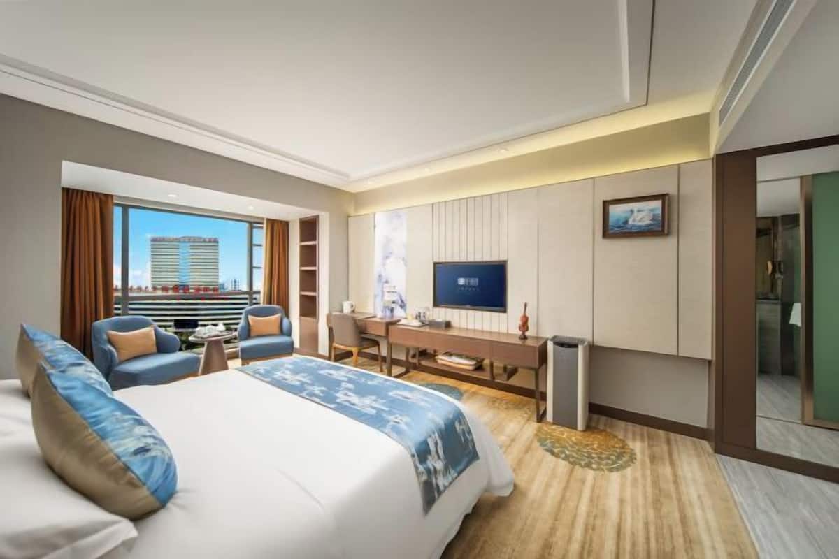 Ein Hotelzimmer mit einem großen Bett, einem Schreibtisch, einem Fernseher und Blick auf eine Stadtlandschaft.