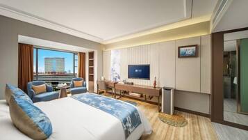 A hotel room with a large bed, a desk, a television, and a view of a cityscape.